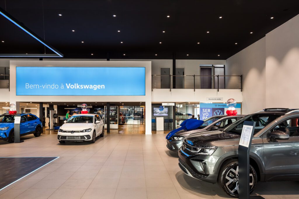 Um showroom de carros com uma placa e carros. - Luiz Volpato Arquitetura