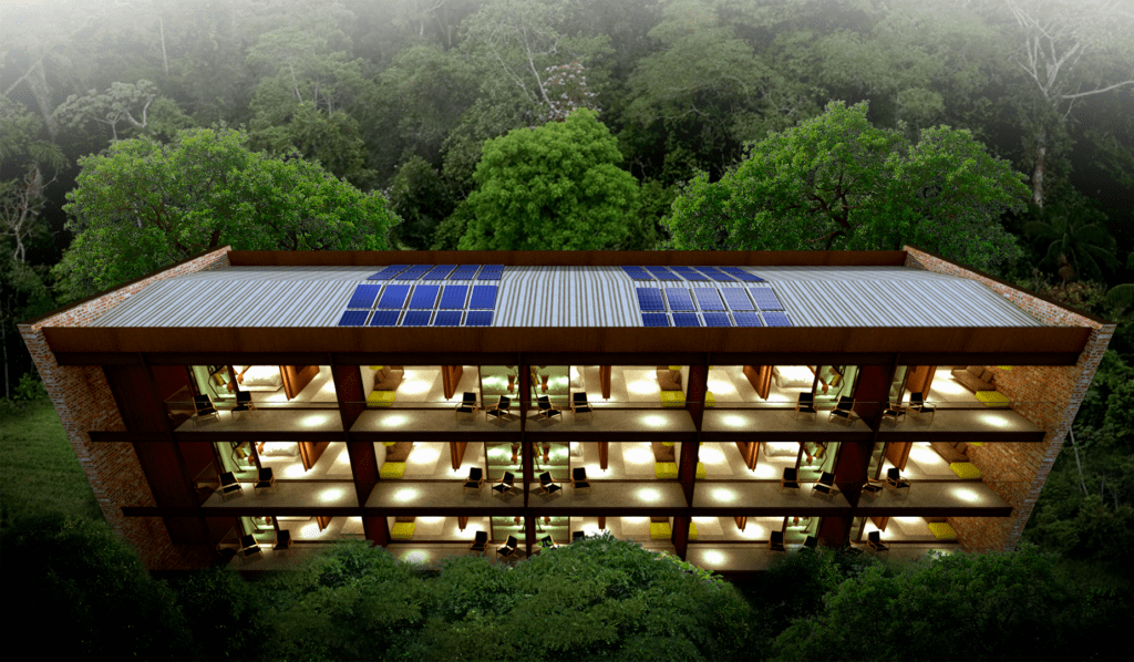 Uma vista aérea de um prédio de três andares em um cenário de floresta exuberante. O prédio possui painéis solares no telhado e varandas em cada andar. Várias janelas revelam a atividade interna, e uma iluminação quente ilumina a estrutura contra a densa vegetação ao redor. - Luiz Volpato Arquitetura