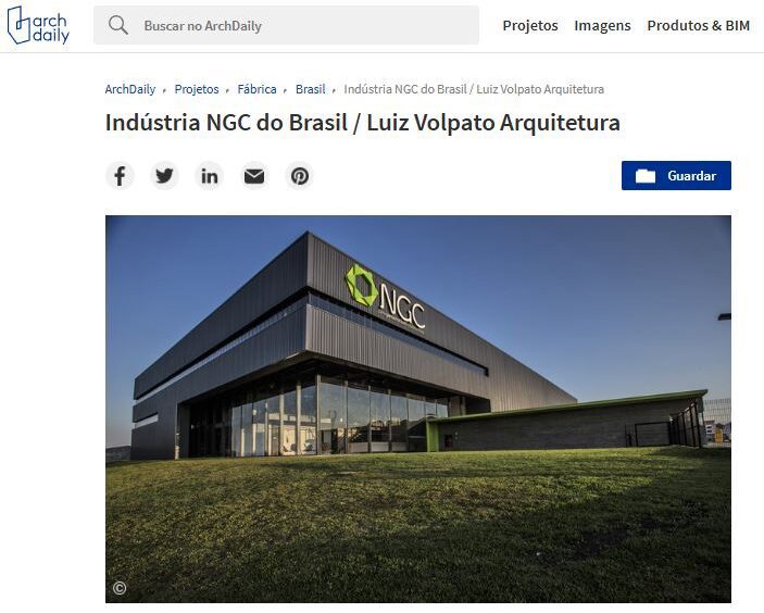 A imagem mostra um edifício industrial moderno com um design elegante e angular e um exterior escuro. Ele apresenta um logotipo verde da NGC na fachada. O edifício é cercado por um gramado bem cuidado e está situado contra um céu azul claro. - Luiz Volpato Arquitetura