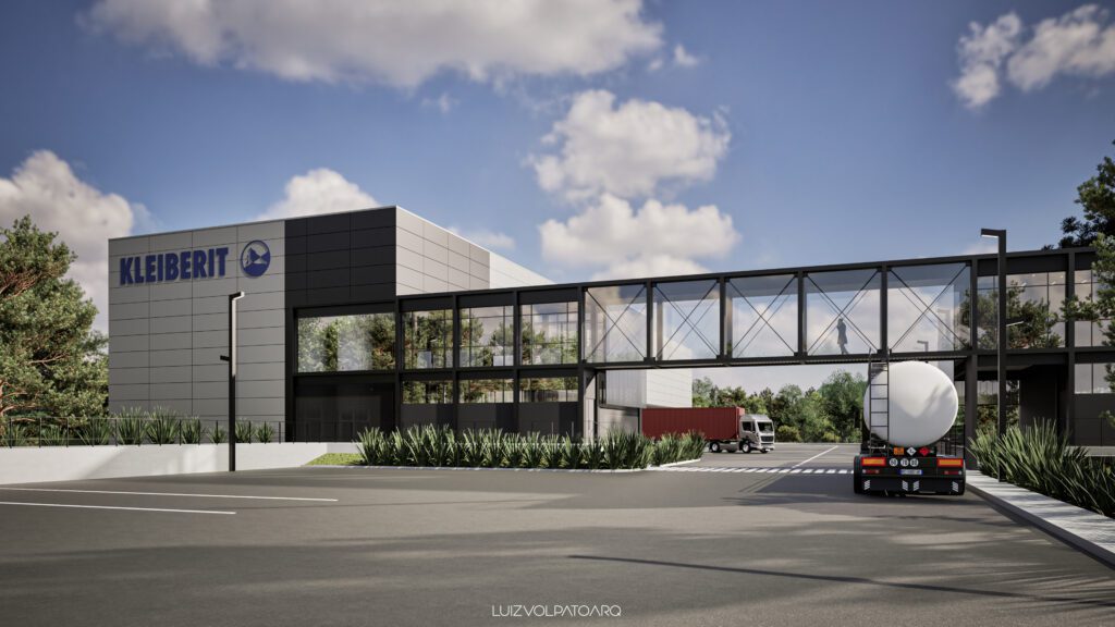 Edifício industrial moderno com o logotipo “KLEIBERIT” à esquerda. Uma passarela envidraçada conecta as duas estruturas. Dois caminhões, um vermelho e outro branco, estão na estrada perto da entrada. Árvores, arbustos, um céu azul límpido e nuvens esparsas cercam a área. - Luiz Volpato Arquitetura