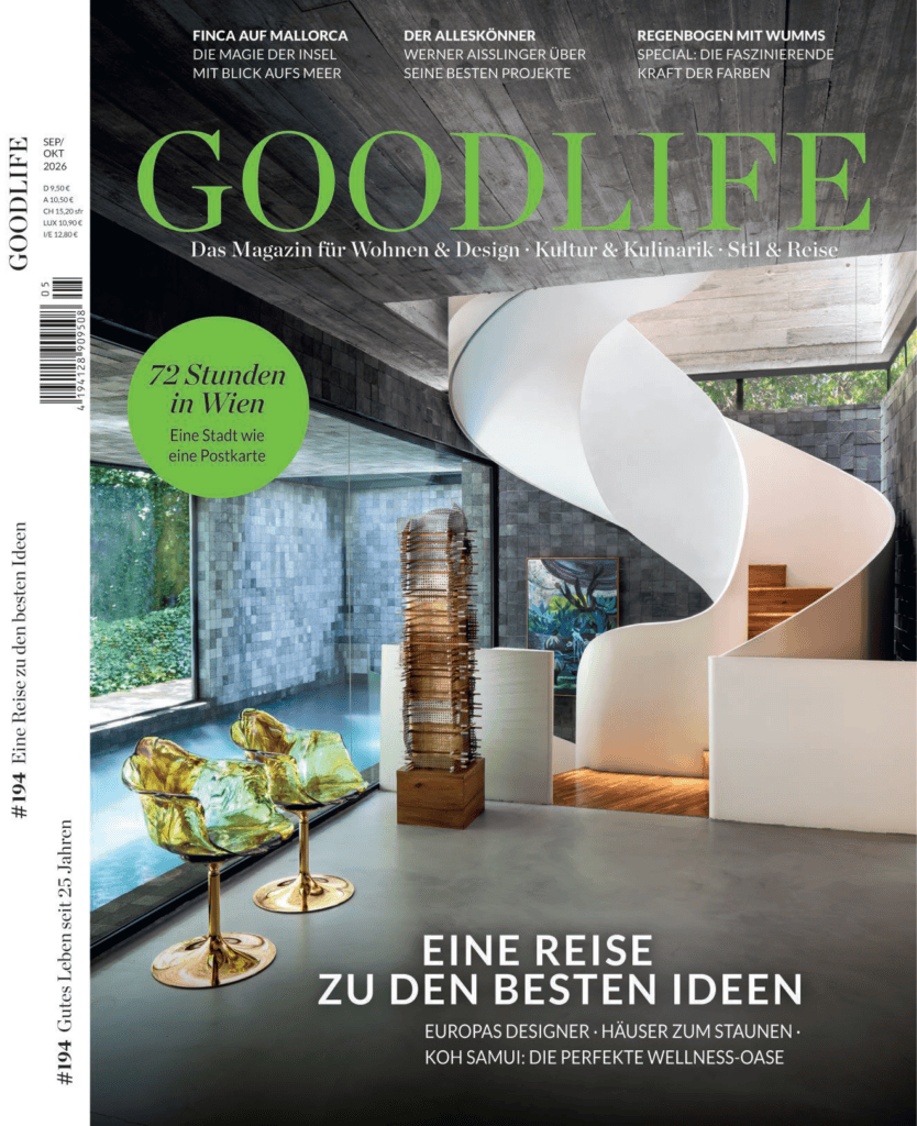 A capa da revista GOODLIFE mostra um interior moderno com uma escada em espiral branca, janelas amplas, duas cadeiras amarelas transparentes e uma vista para uma área externa arborizada. O texto destaca temas relacionados a viagens e design. O design é elegante e contemporâneo. - Luiz Volpato Arquitetura